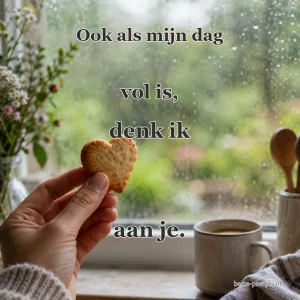 Een hand houdt een hartvormig koekje bij een regenachtig raam en een warme kop thee.