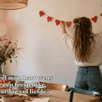Een meisje hangt een slinger van rode papieren hartjes op.