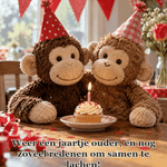 Twee pluchen aapjes zitten samen bij een verjaardagscupcake.